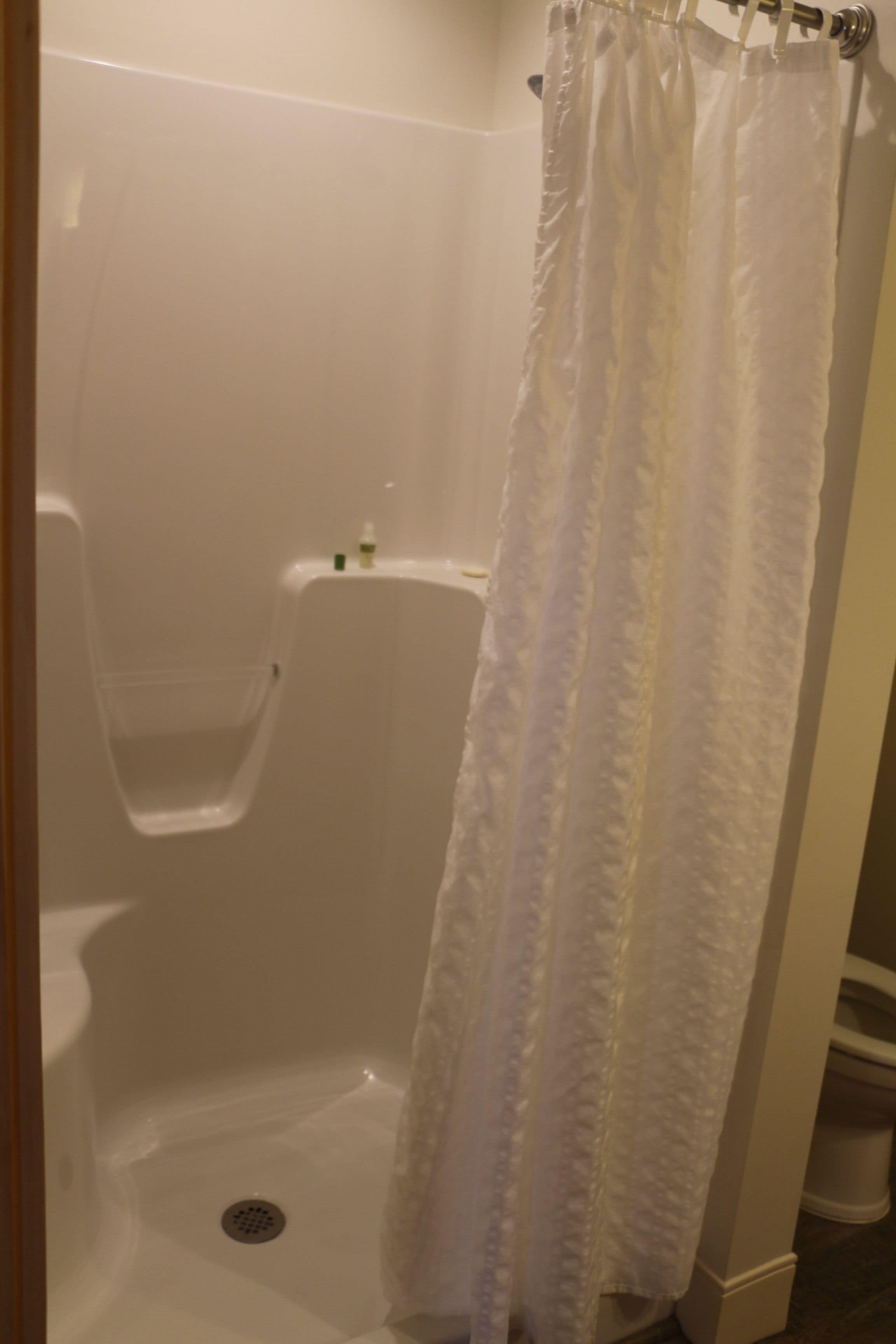 Una bañera blanca con cortina de ducha, un pequeño estante con artículos de aseo y un desagüe.
