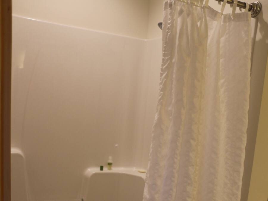 Una bañera blanca con cortina de ducha, un pequeño estante con artículos de aseo y un desagüe.