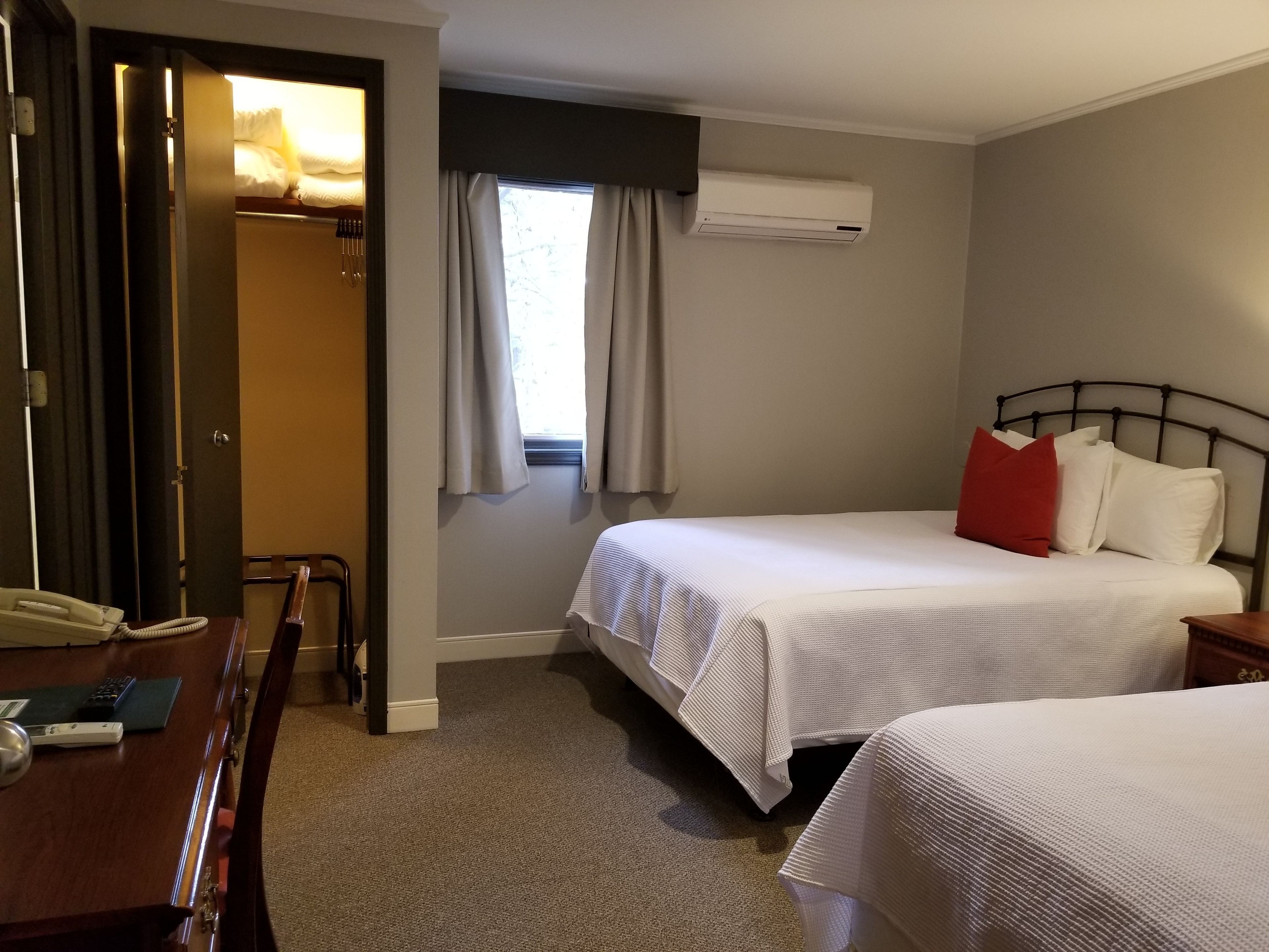 A hotel room with two beds, a desk with a telephone, and an air conditioning unit on the wall.