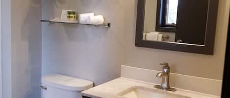 A bathroom with a toilet, a sink, a mirror, and shelves with toiletries.
