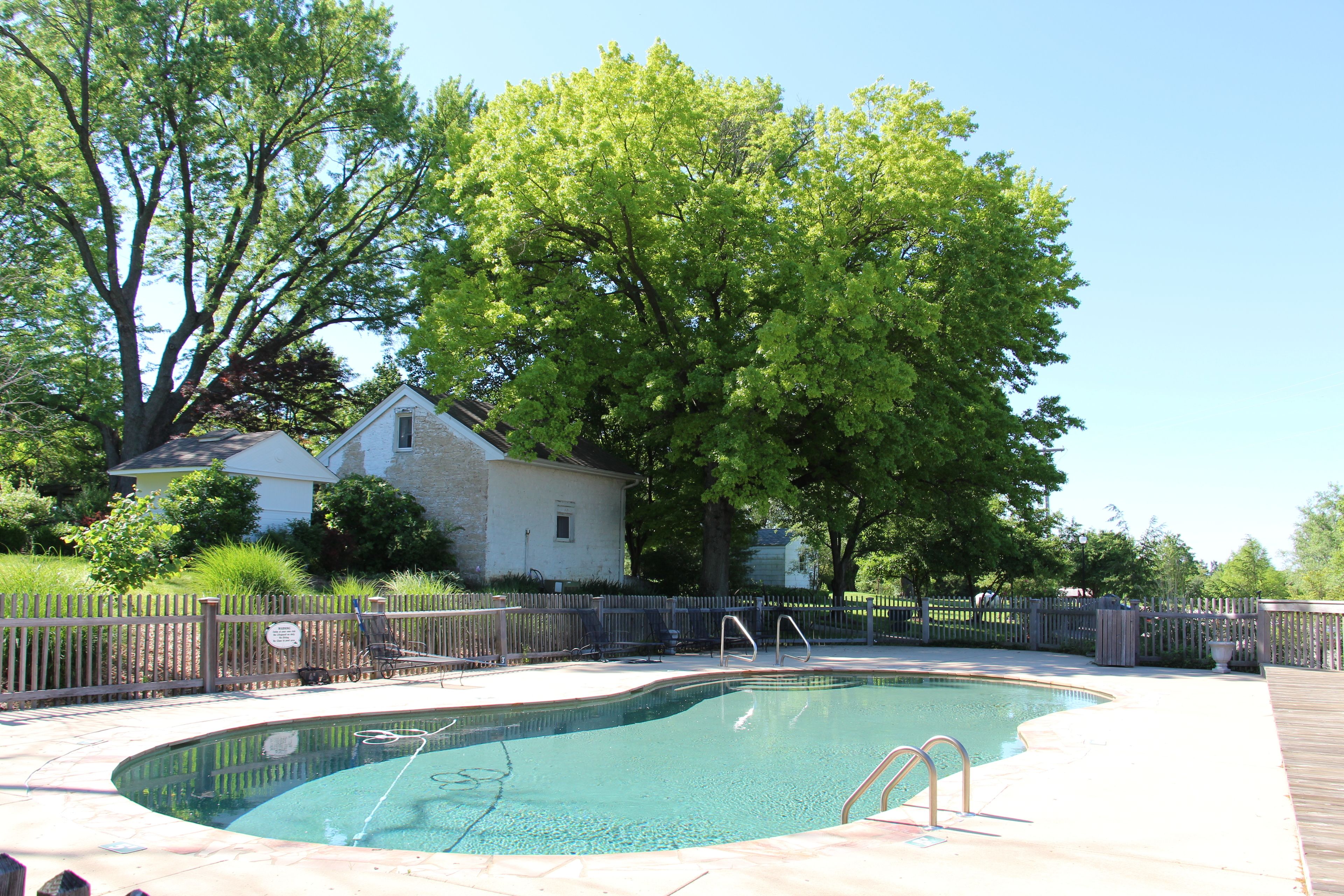 Una piscina con bordo in legno, una recinzione e una casa sullo sfondo.
