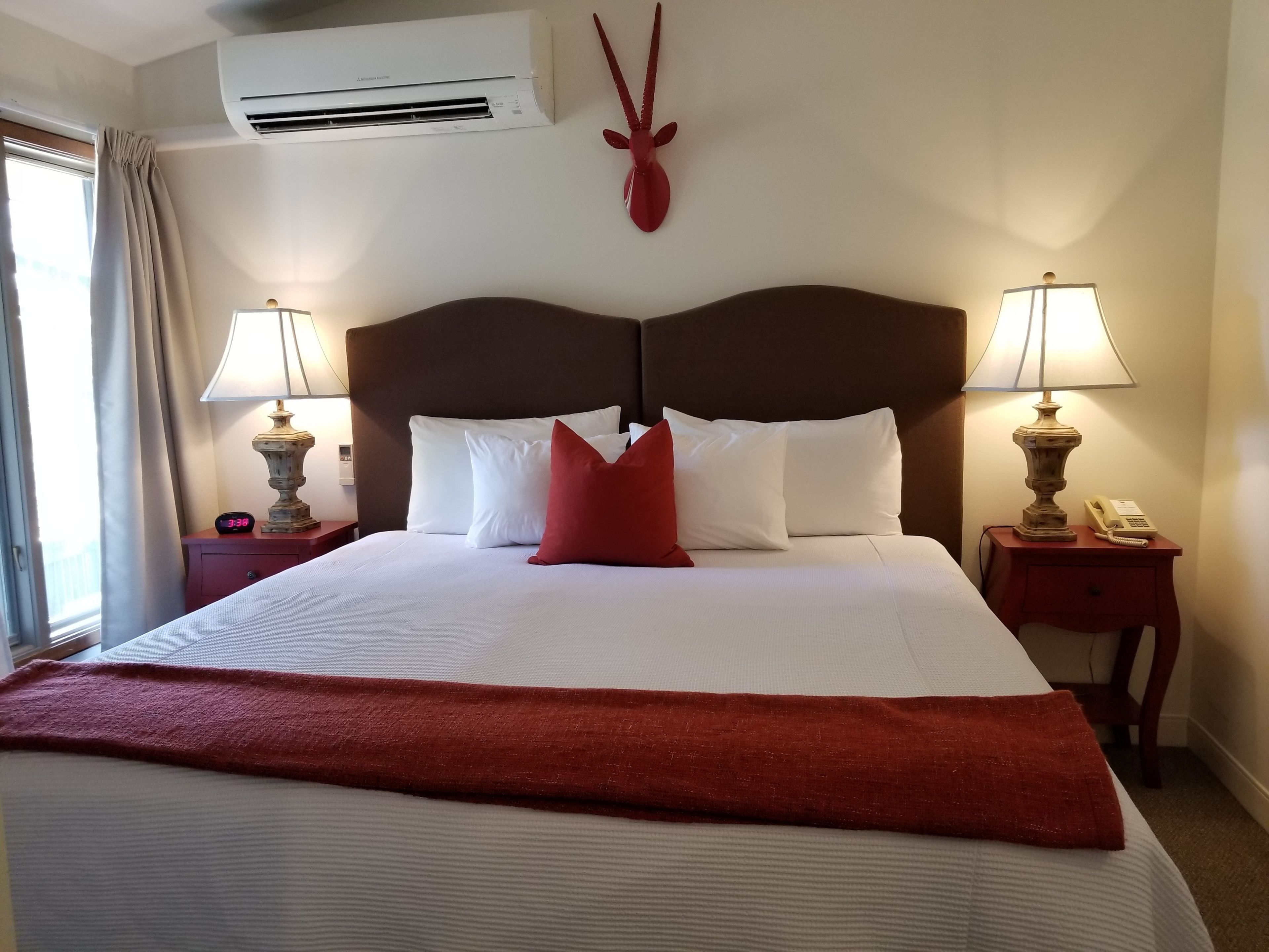 A hotel room with a large bed, two bedside tables with lamps, a wall-mounted telephone, and a decorative antelope head.