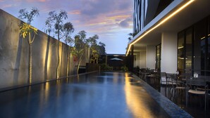 Un couloir d’hôtel moderne avec une piscine, un espace de détente extérieur et une vue sur le ciel.