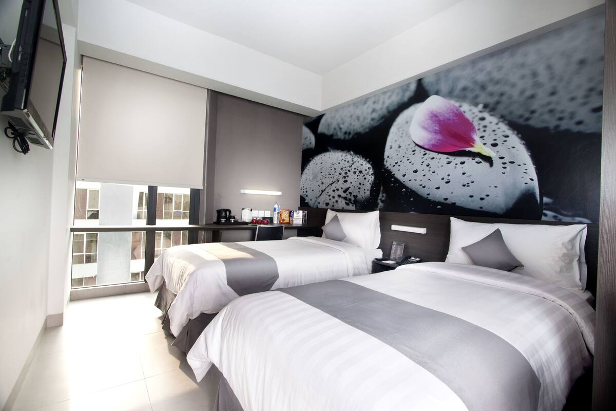 Ein modernes Hotelzimmer mit zwei Betten, einem großen Fenster, einem Flachbildfernseher und einem Wandbild.