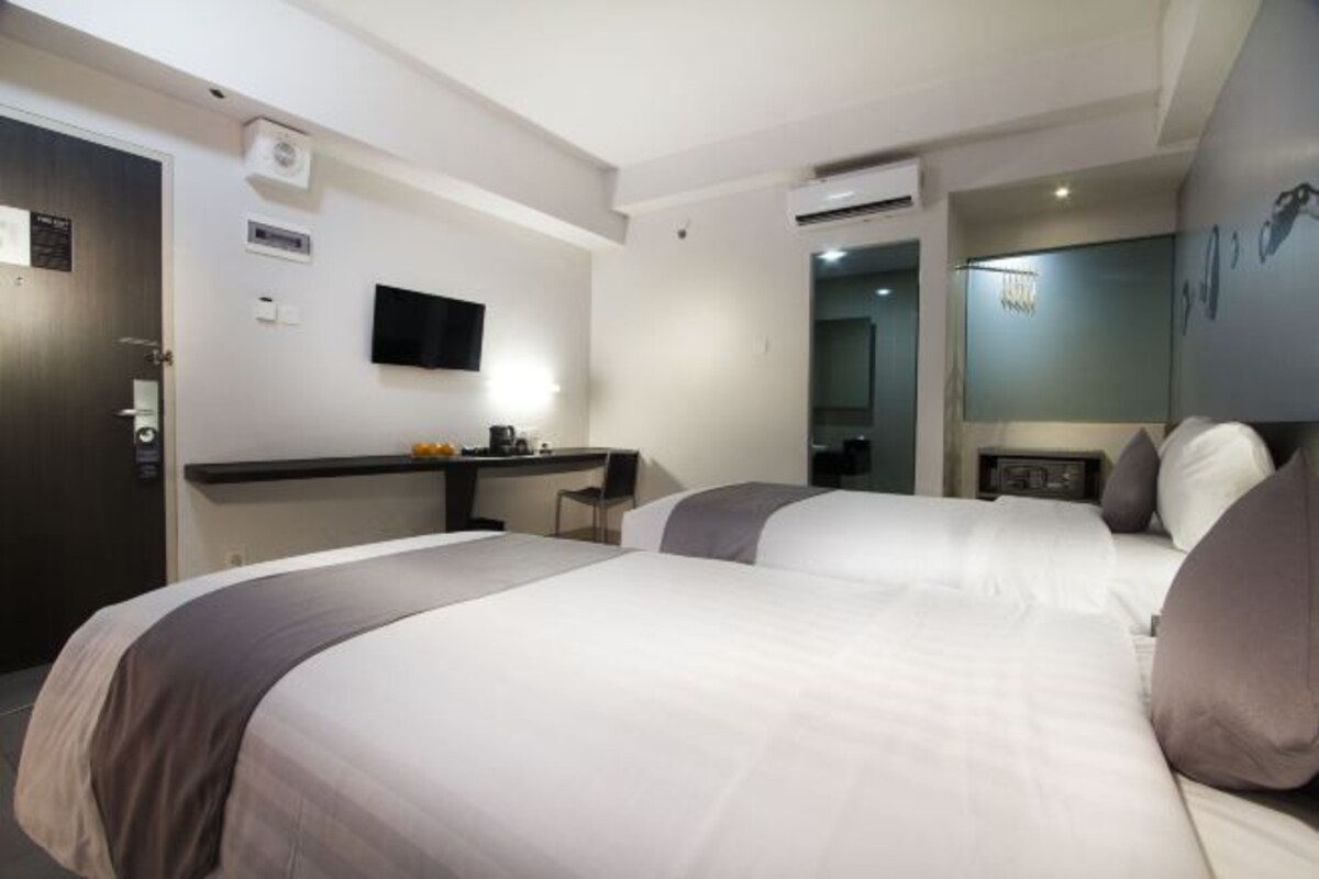 A hotel room with two beds, a desk, a flat-screen TV, and a mirror.