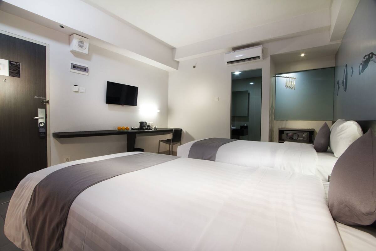 Ein Hotelzimmer mit zwei Betten, einem Schreibtisch, einem Flachbildfernseher und einem Spiegel.