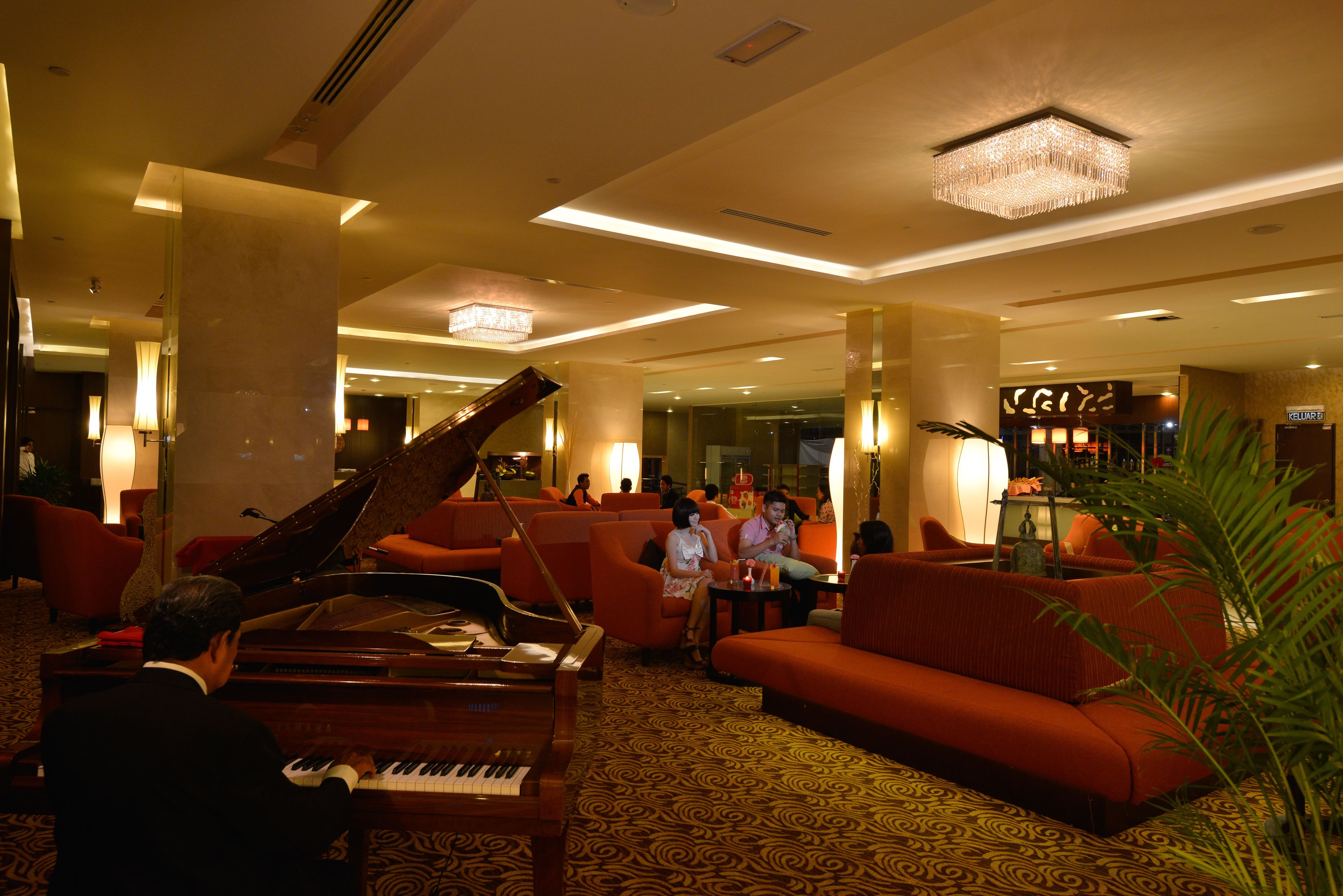 A grand piano in a lobby with red sofas and a chandelier.