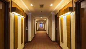 Un largo y estrecho pasillo de hotel con puertas a ambos lados, suelo alfombrado e iluminación en el techo.