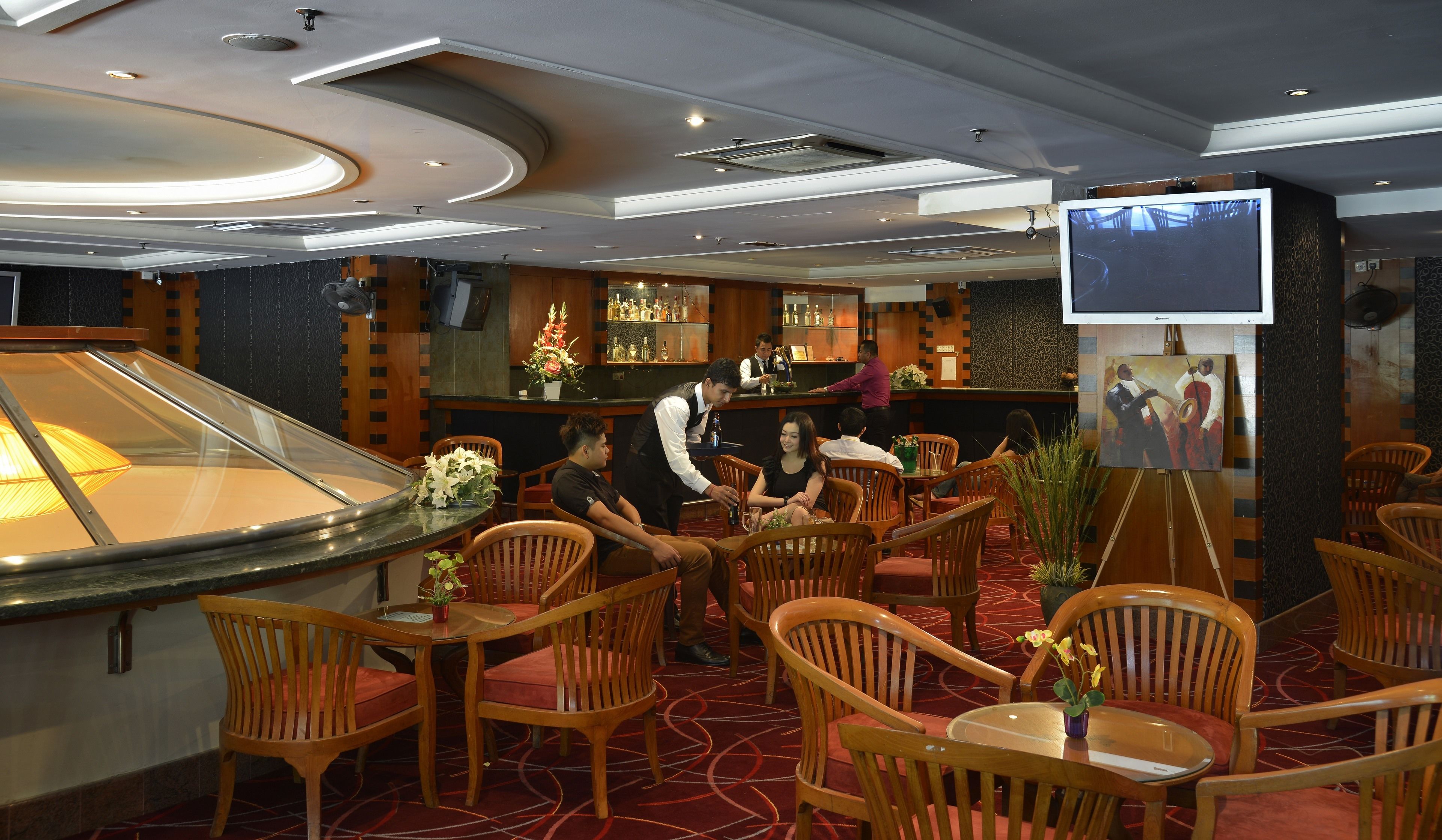 Un restaurante con sillas y mesas de madera, una zona de bar y una pantalla de televisión.