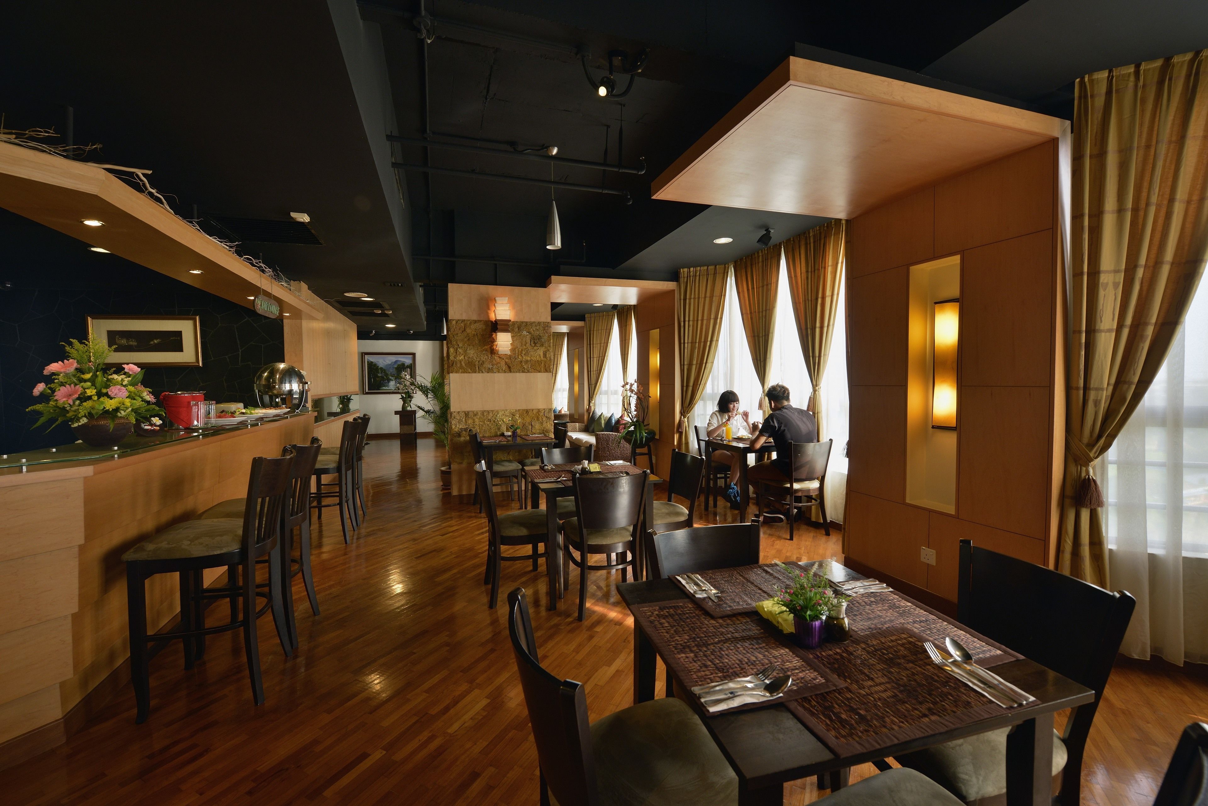 A restaurant with wooden flooring, tables with place settings, and a bar area with a counter and stools.
