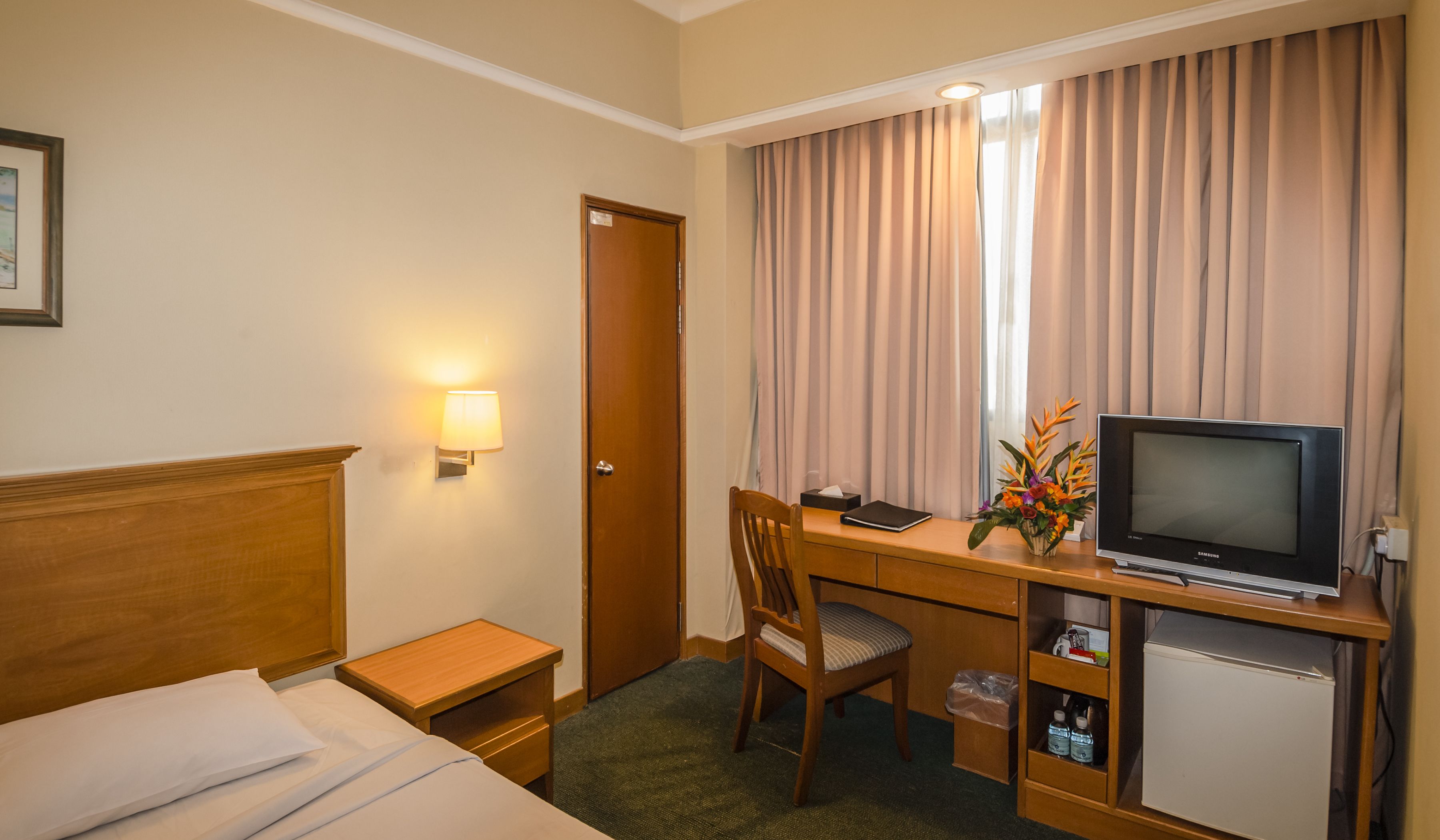Habitación de hotel con cama, escritorio con televisor, silla, mesita y lámpara.
