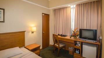 Habitación de hotel con cama, escritorio con televisor, silla, mesita y lámpara.
