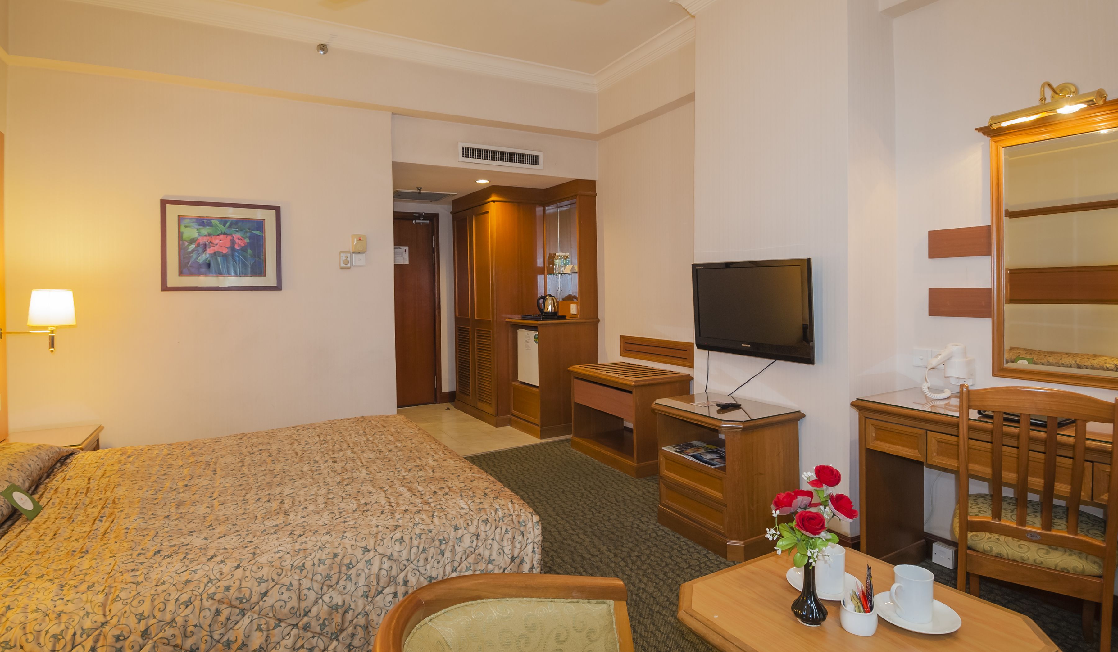 A hotel room with a bed, desk, chair, TV, and a mirror.