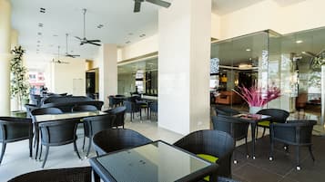 A modern indoor dining area with glass tables and wicker chairs, ceiling fans, and a view of the city through large windows.