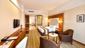 Habitación de hotel con cama, escritorio con silla, televisión, mesita de noche con lámpara y un cuadro en la pared.
