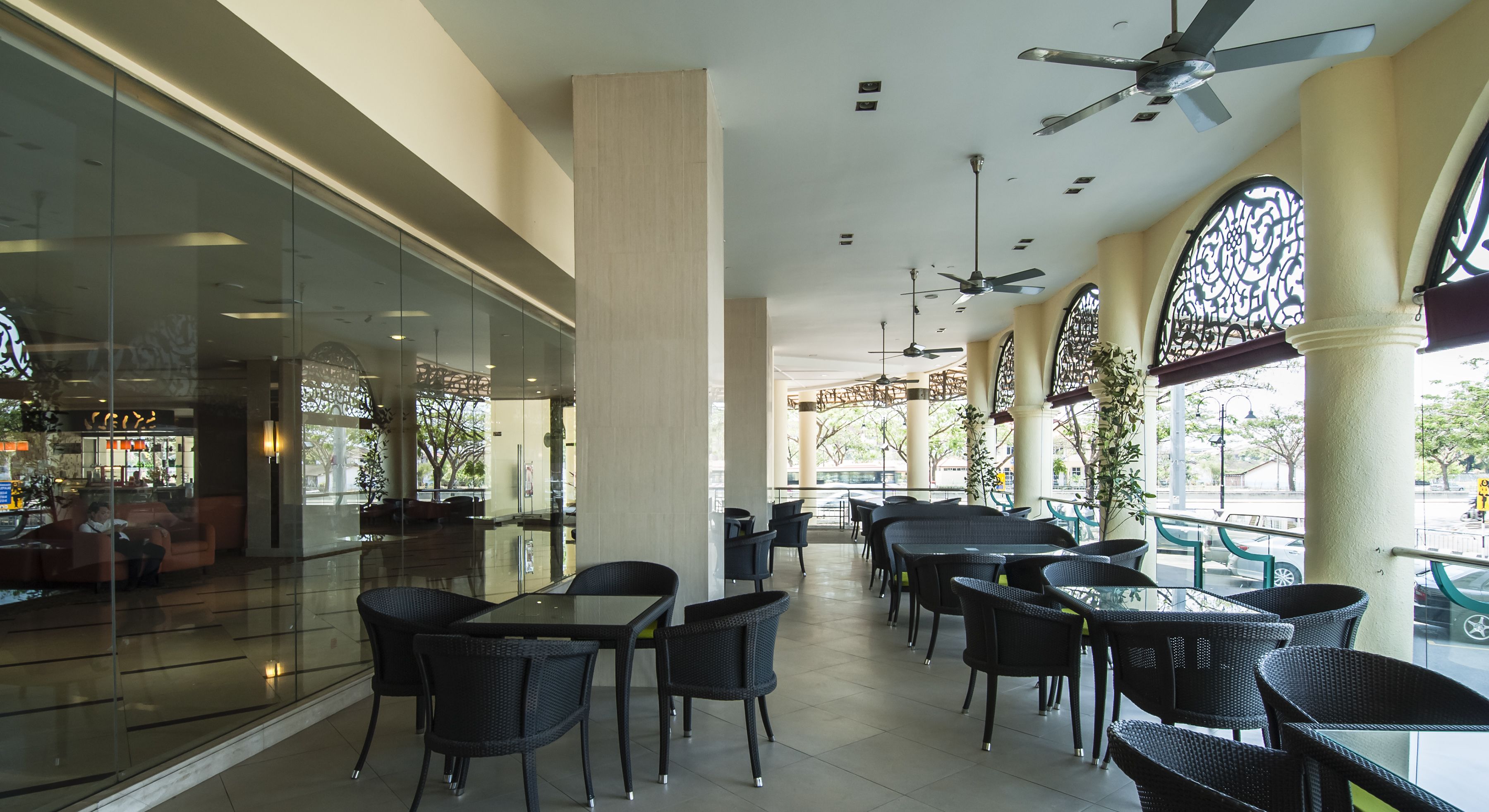 Un amplio espacio interior con paredes de vidrio, varias mesas y sillas, ventiladores de techo y columnas decorativas.