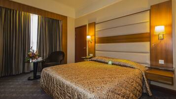 Una habitación de hotel con una cama grande, una silla, una mesita con un florero y una mesita de noche con una lámpara.