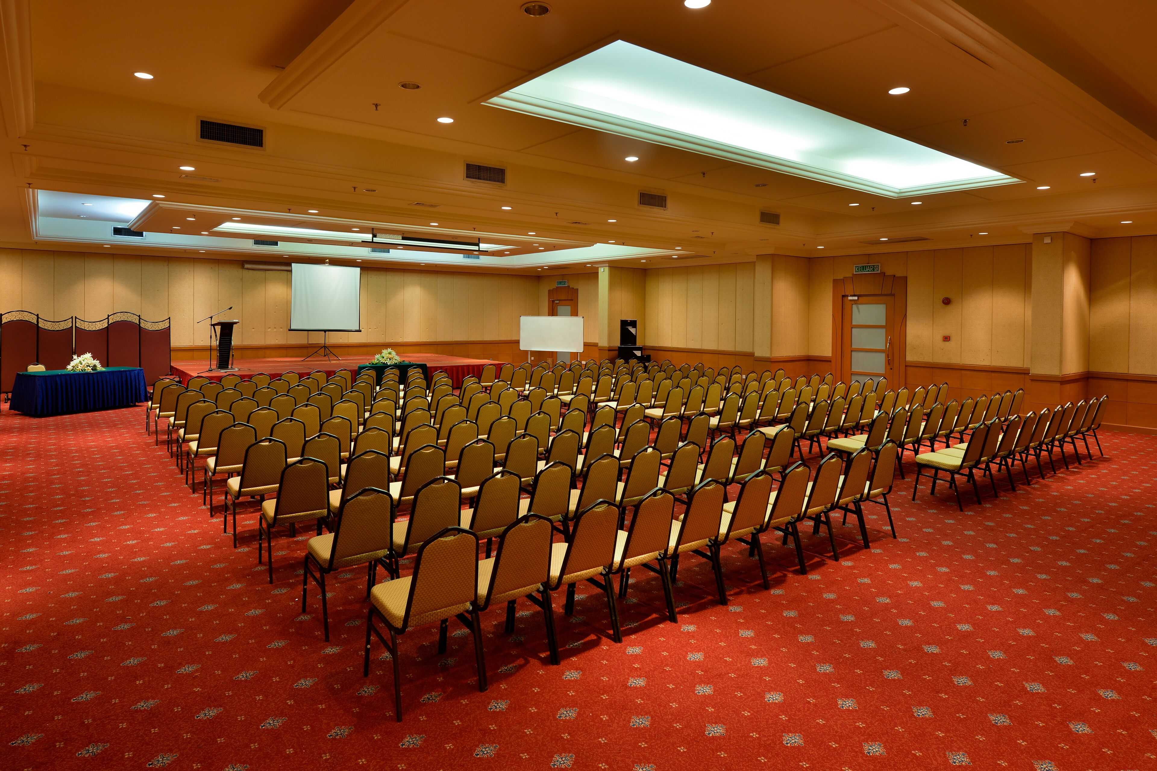 A large conference room with rows of chairs, a podium, a screen, and a carpeted floor.