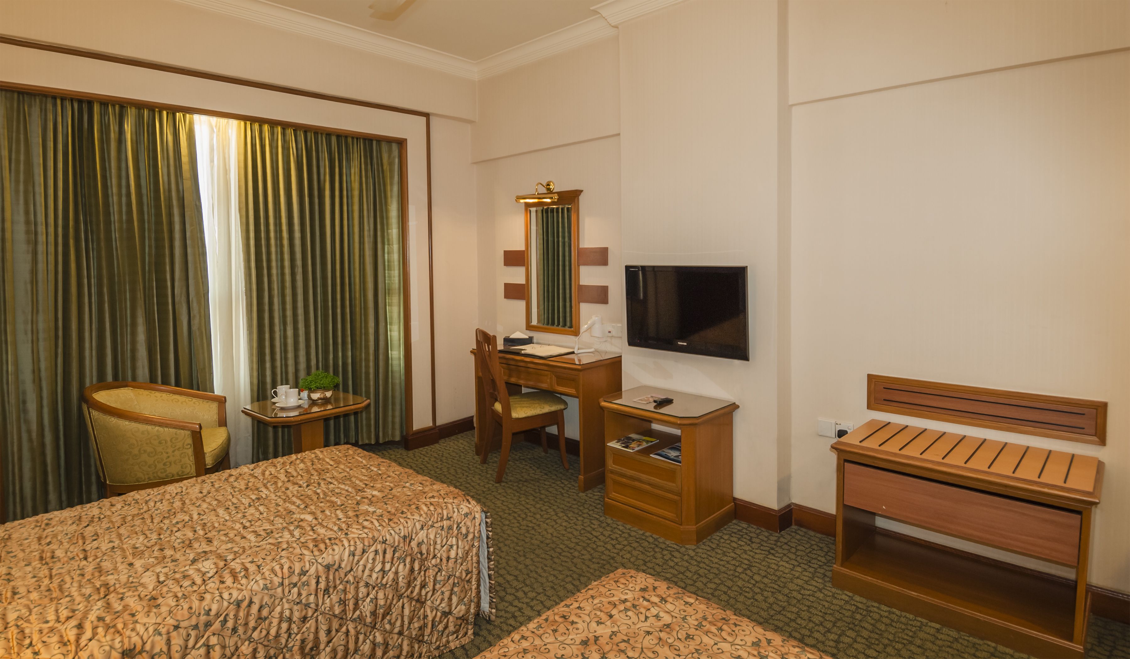 Habitación de hotel con cama, escritorio, silla, televisión y ventana con cortinas.