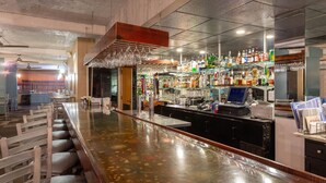 Een bar met een lange toonbank, barstoelen en een verscheidenheid aan flessen en glazen op planken.