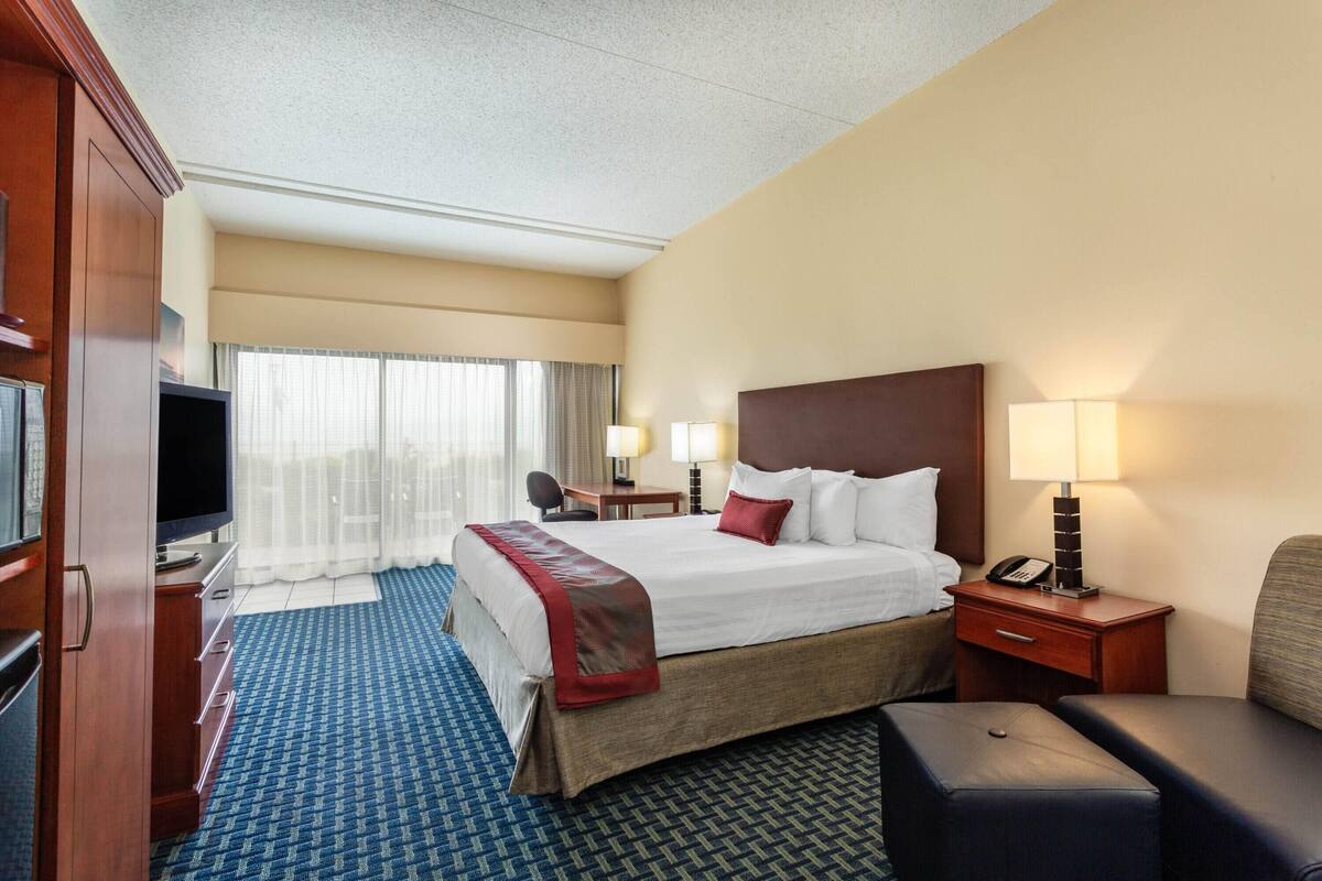 Habitación de hotel con una cama grande, un escritorio, una silla, un televisor y una lámpara.