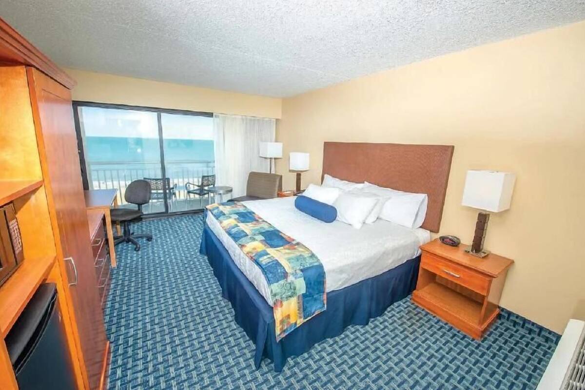 Habitación de hotel con cama, escritorio, silla, una mesita y vista al océano.