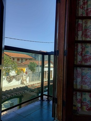 A balcony with a view of a residential street, a metal railing, and a door with floral curtains. - Pousada Alecrim Dourado (Paraty)