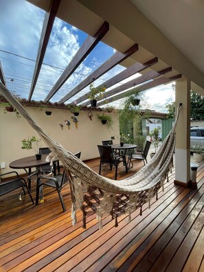 A covered patio with a hammock, wooden flooring, a table with chairs, and potted plants. - Pousada Alecrim Dourado (Paraty)