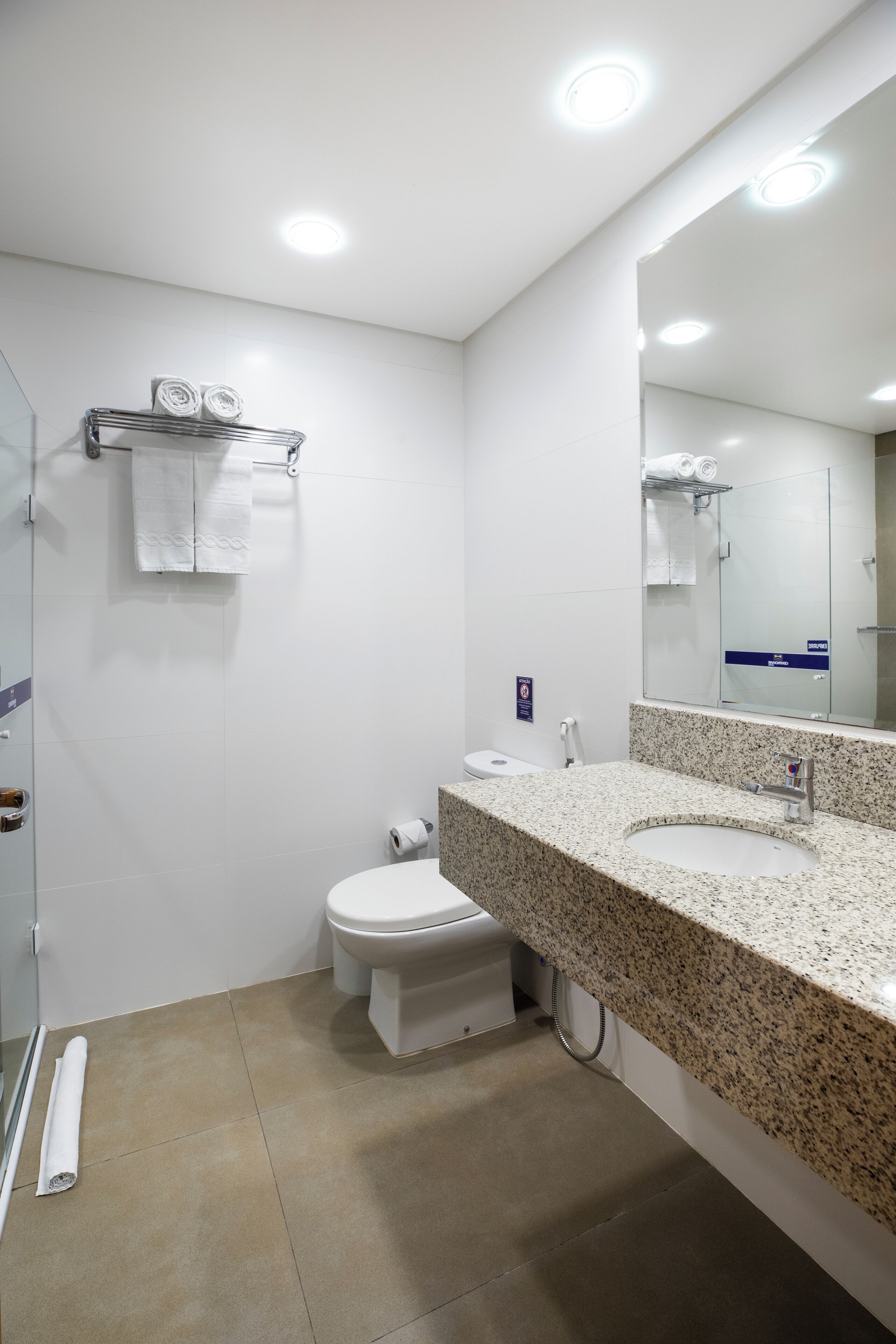 A modern bathroom with a granite countertop, white fixtures, and a large mirror.
