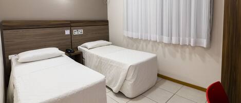 Habitación de hotel con dos camas individuales, cabecera de madera, teléfono junto a la cama, aire acondicionado instalado en la pared y una silla roja.