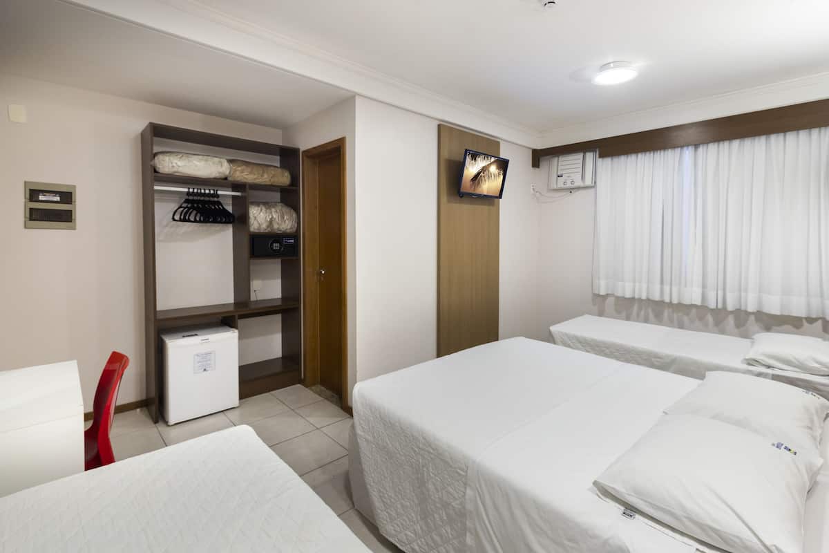 A hotel room with two beds, a wardrobe, a small desk, and a television.