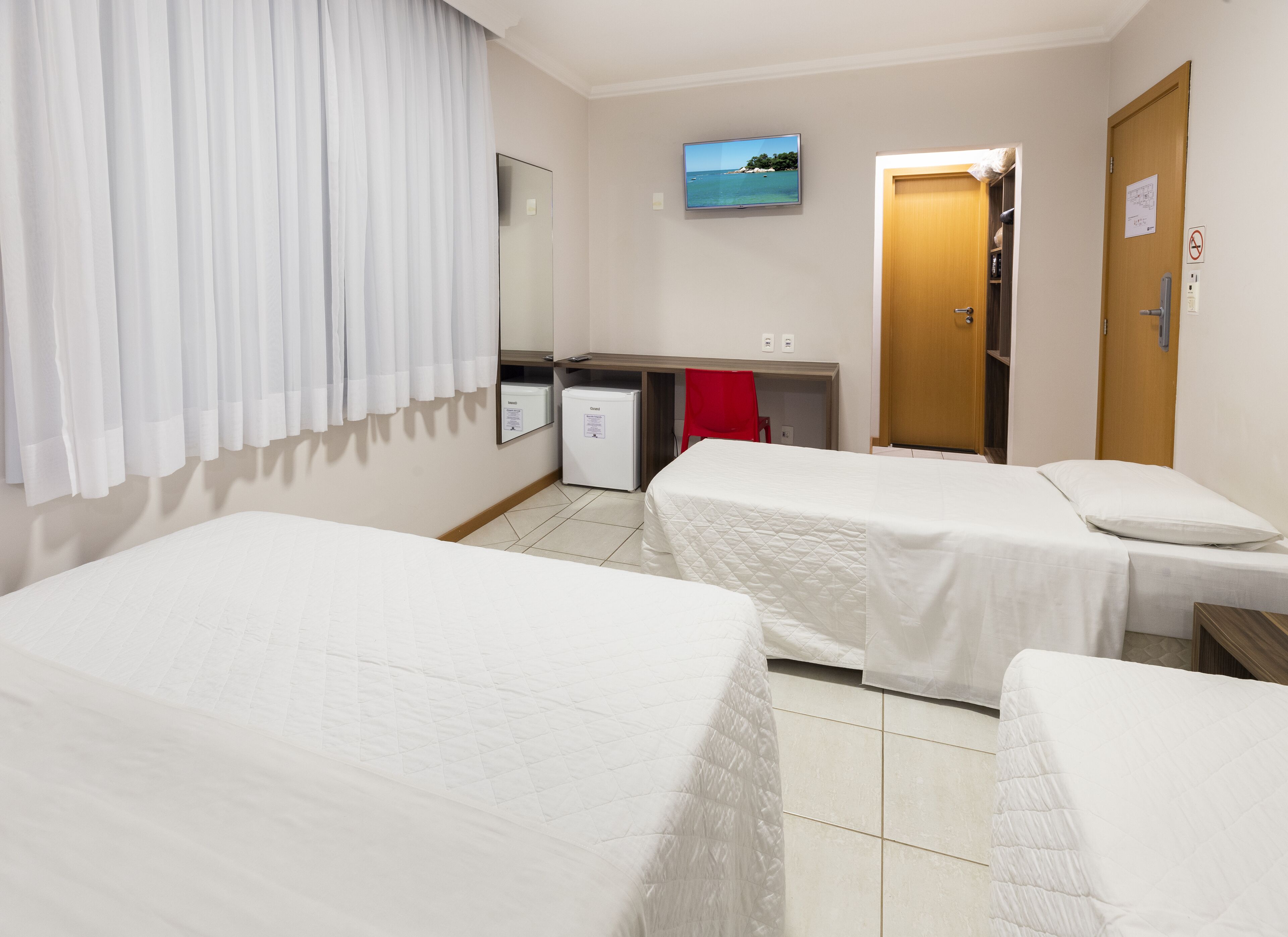 Une chambre d’hôtel avec deux lits simples, un petit bureau avec un ordinateur, un téléviseur fixé au mur et un espace douche.