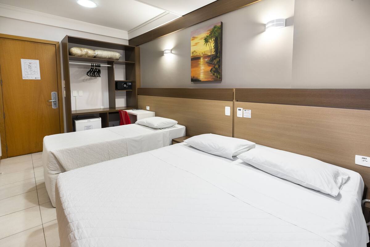 A hotel room with two beds, a wardrobe, a desk, and a painting on the wall.