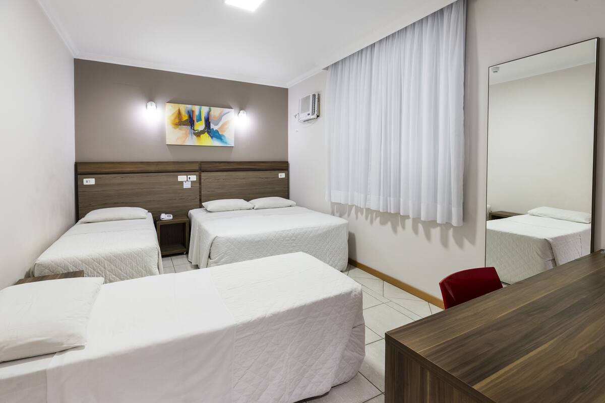 A hotel room with two single beds, a wooden headboard, a large mirror, a desk, and a red chair.