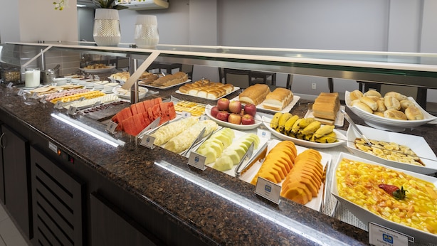 Un bufé con diversas opciones de comida, entre ellas frutas, pan y pastelería.