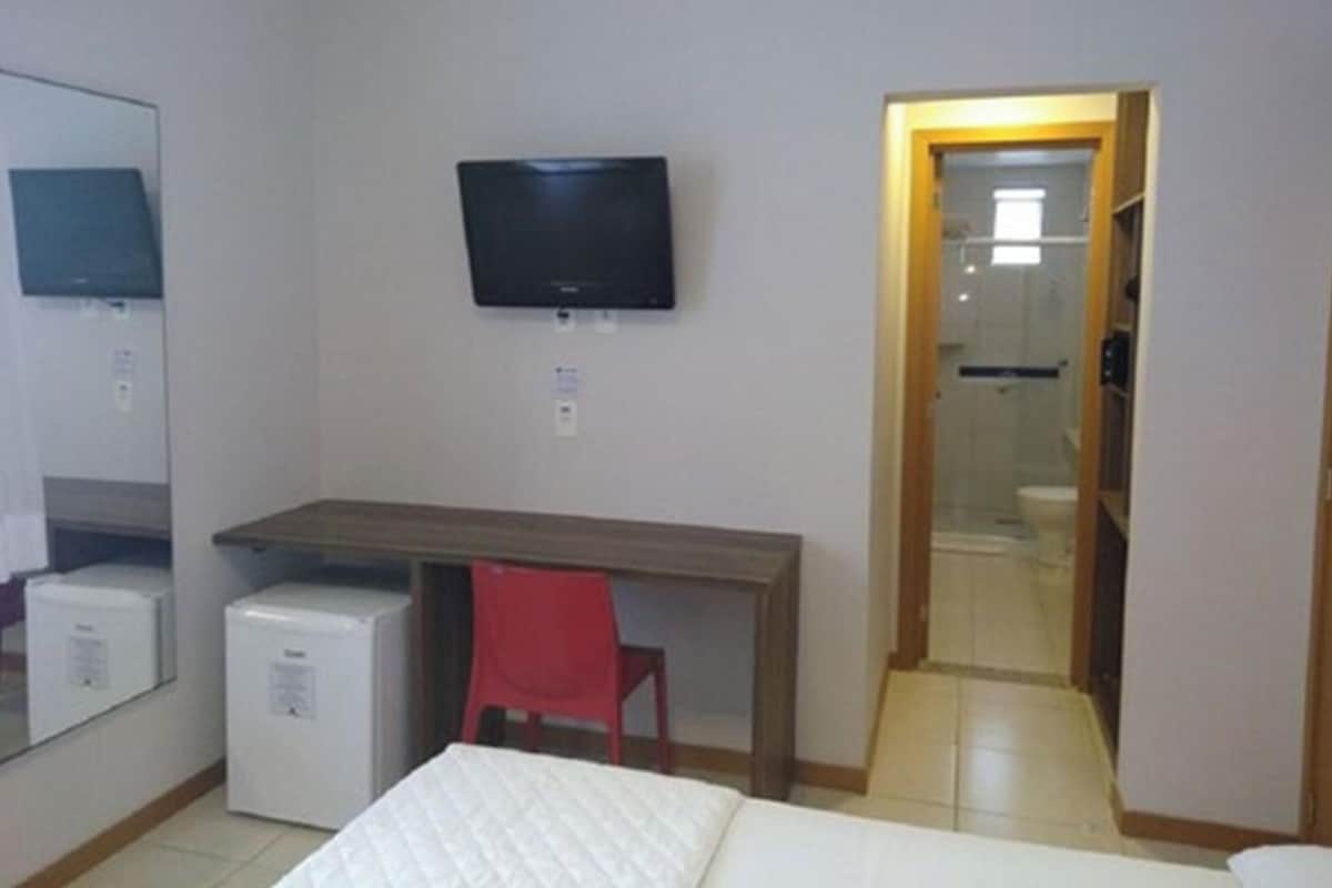 Un dormitorio con cama, escritorio, silla, televisor y un refrigerador pequeño.
