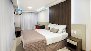 Una habitación de hotel moderna con una cama grande, un escritorio, una silla, un televisor montado en la pared y un cabecero de madera.
