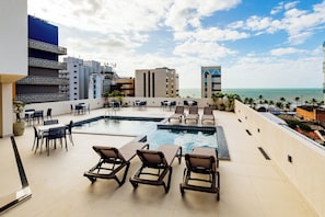 A rooftop pool area with lounge chairs and tables, overlooking a beach and cityscape. - El Aram Beach Express (Maceió)