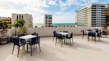 Terraço ao ar livre com mesas e cadeiras, com vista para a água e edifícios.