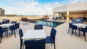 A rooftop pool area with lounge chairs, tables, and chairs.