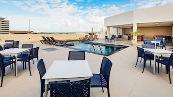 Área de piscina no terraço com espreguiçadeiras, mesas e cadeiras.