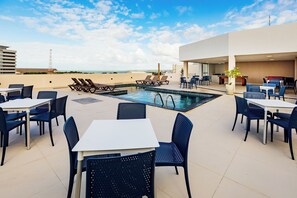 Área de piscina no terraço com espreguiçadeiras, mesas e cadeiras.