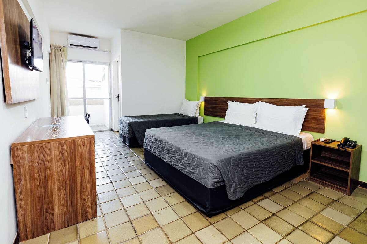 A hotel room with two beds, a wooden desk, a TV, and a green accent wall.