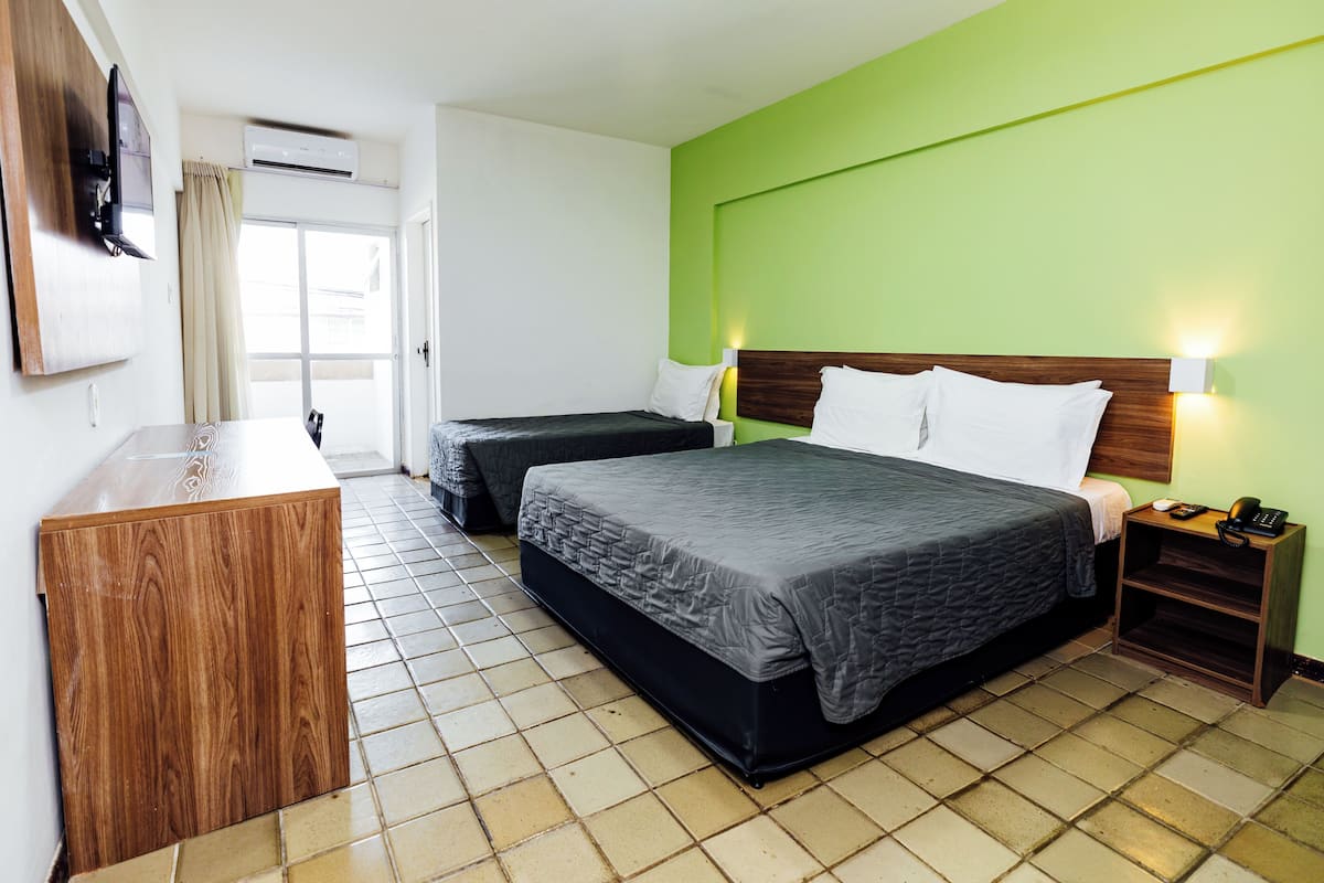 Habitación de hotel con dos camas, un escritorio de madera, un televisor y una pared de acento verde.