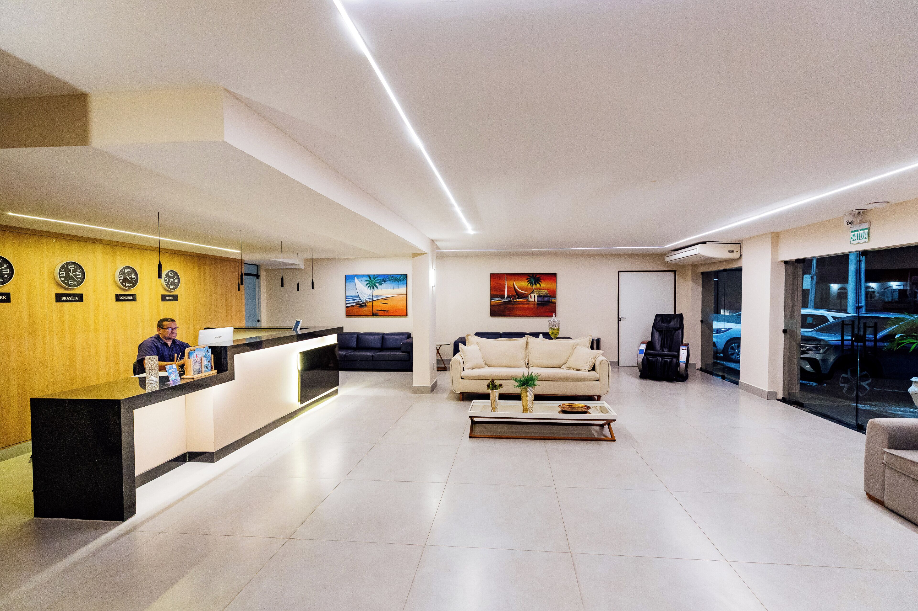 A modern hotel lobby with a reception desk, a sofa, a coffee table, and artwork on the walls.
