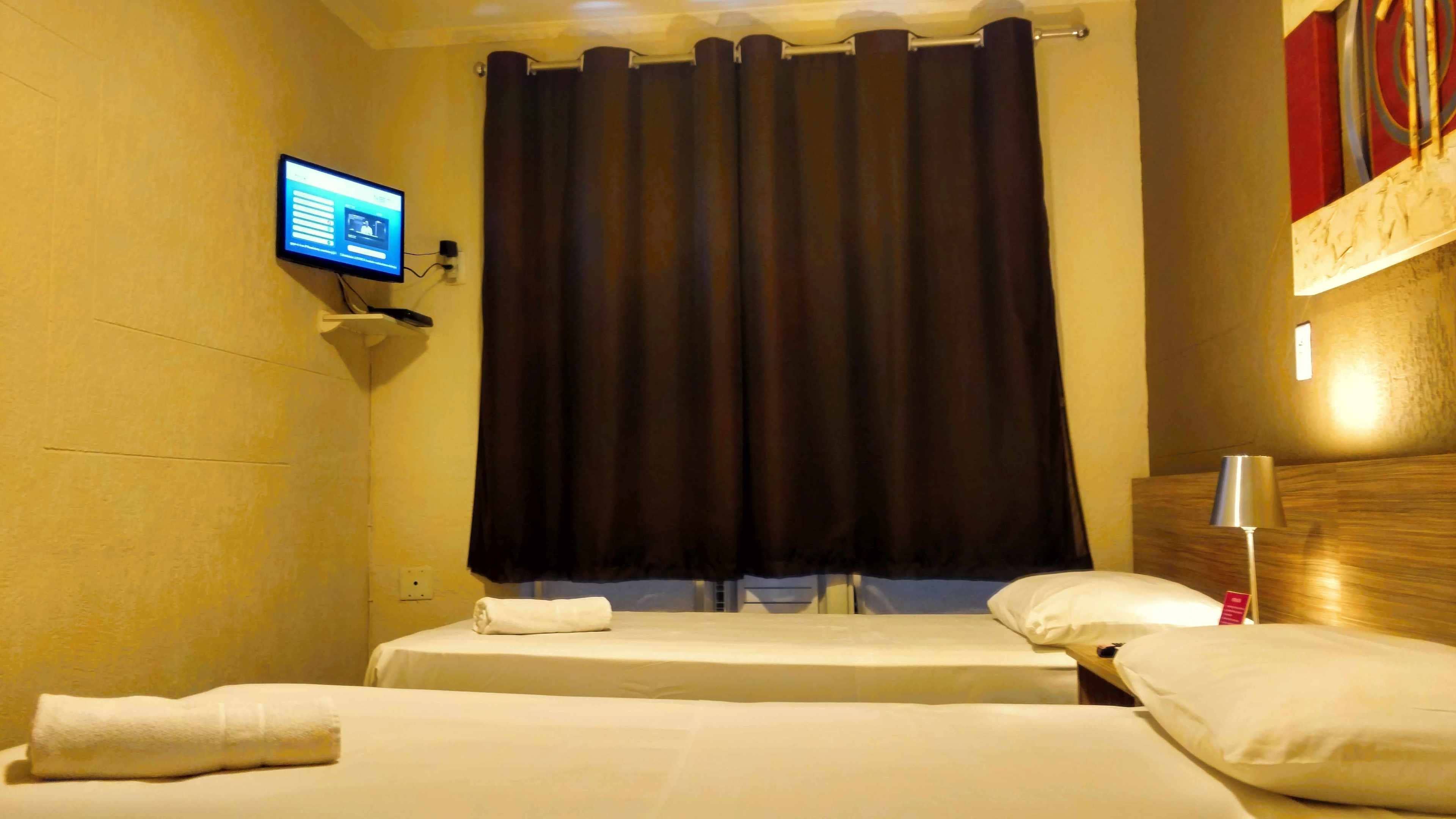 A hotel room with two beds, a television on the wall, and a curtain.