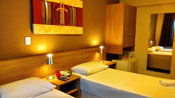 A hotel room with two beds, bedside lamps, a wooden headboard, a small desk with a telephone, and a mirror.