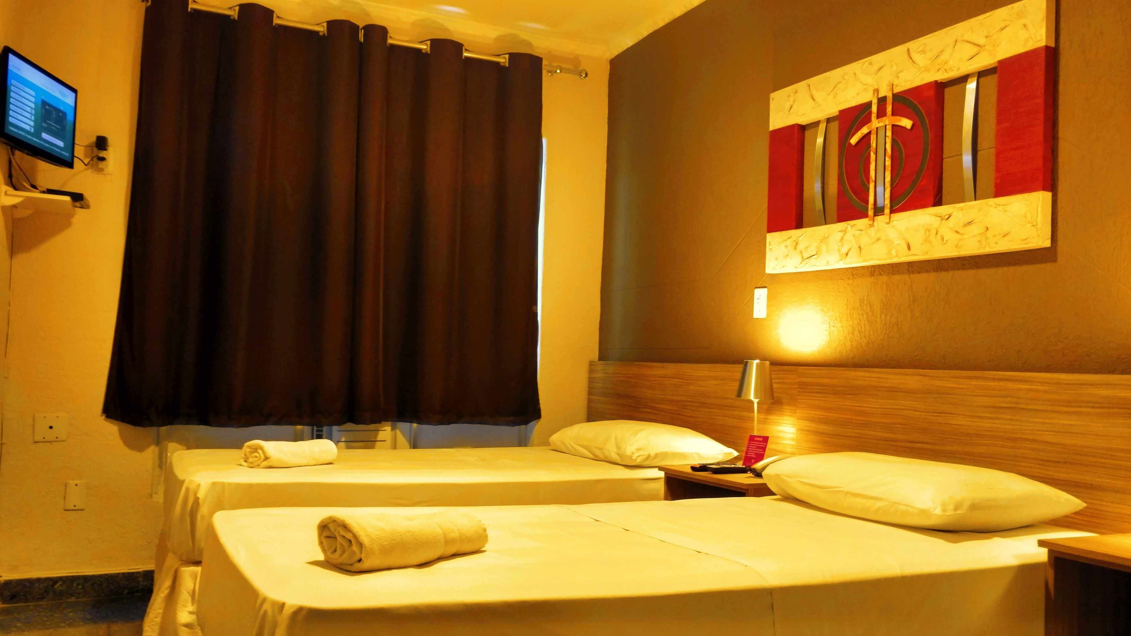Una habitación de hotel con dos camas, un televisor en la pared, un cuadro y una lámpara.