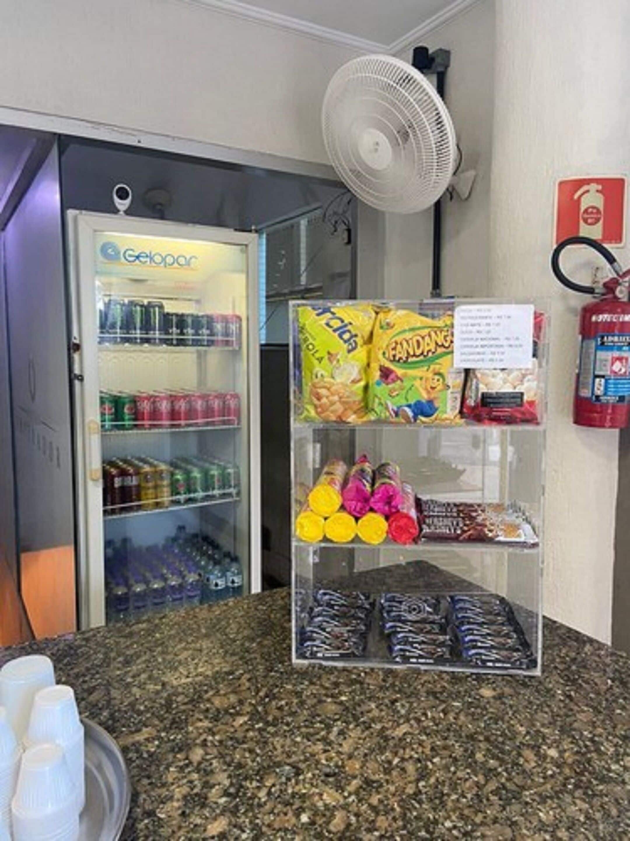 Een automaat met snacks en drankjes, een brandblusser aan de muur en een ventilator aan het plafond.