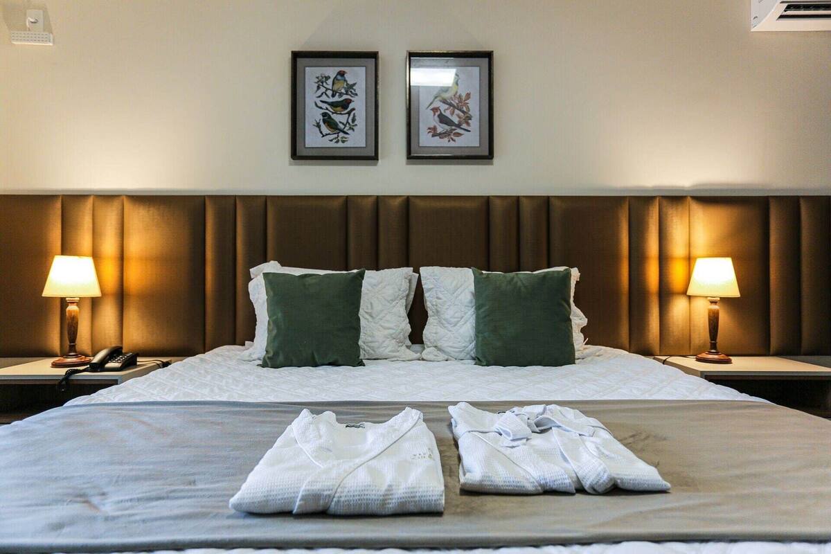 A hotel room with a large bed, two nightstands, two lamps, and two framed pictures on the wall.